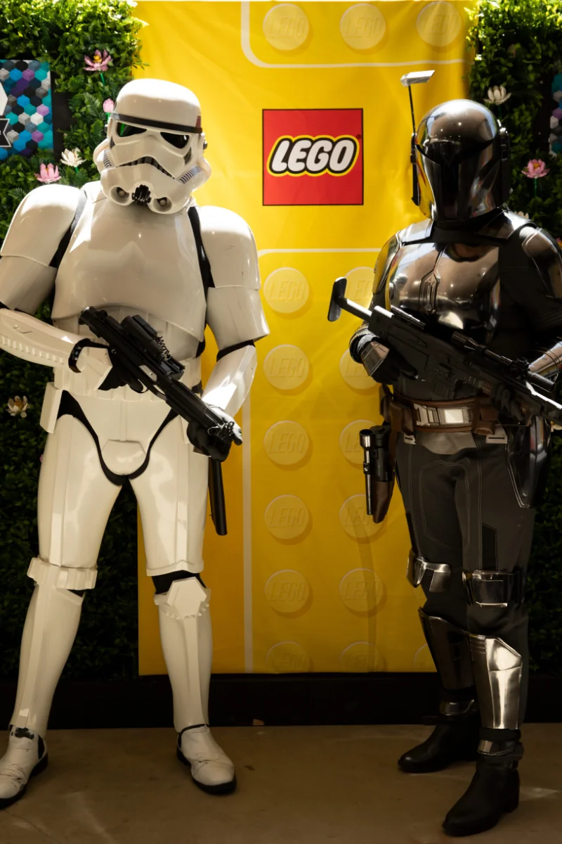 A Storm Trooper from the 501st, and a Mandalorian from the Sandhawk Clan posing for a photo in front of a LEGO banner