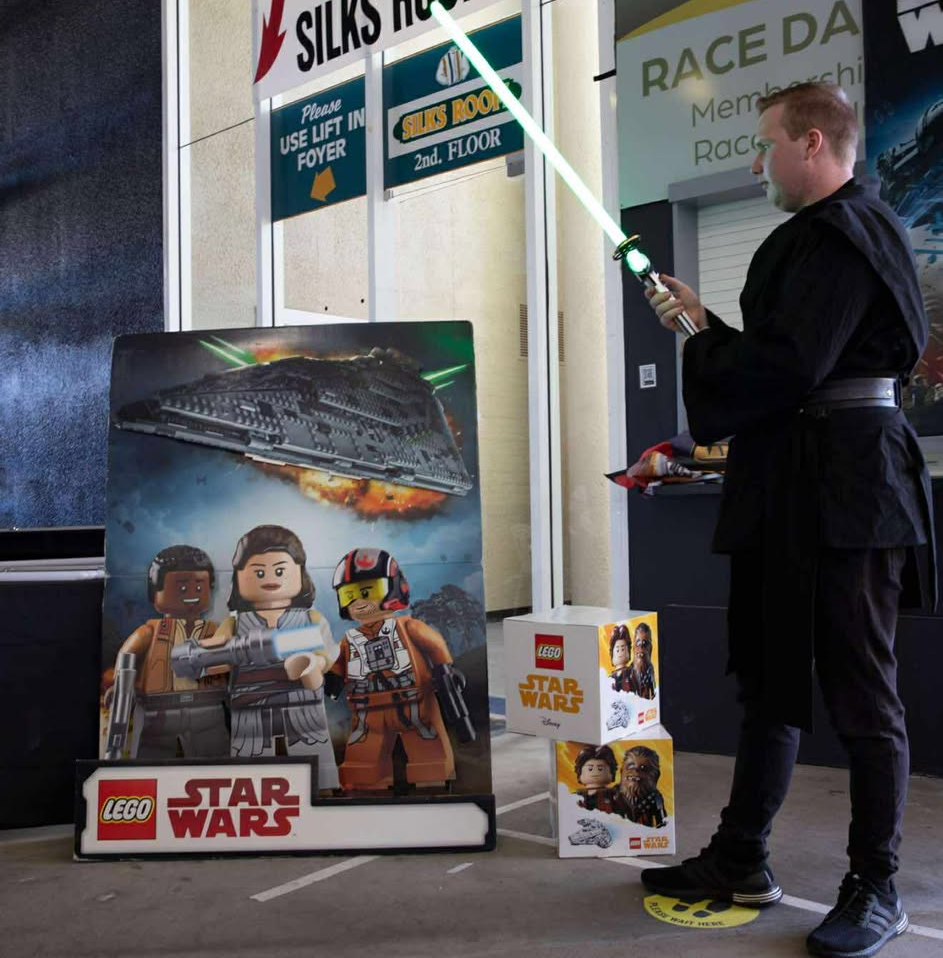 A person in Jedi garb holding a lightsabre in front of a LEGO Star Wars poster